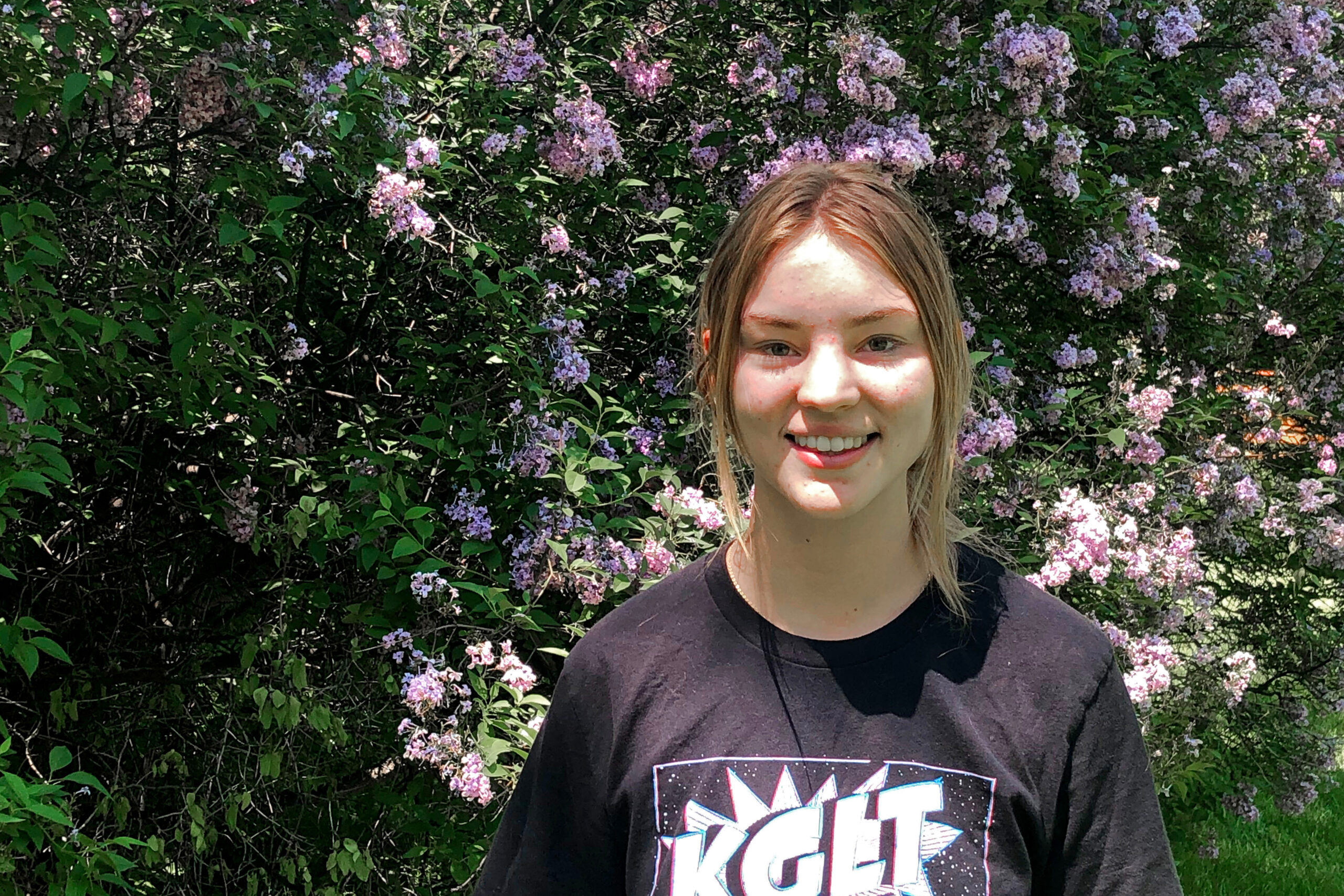 A photo shows Claire Vlases standing outside by a flowering shrub.