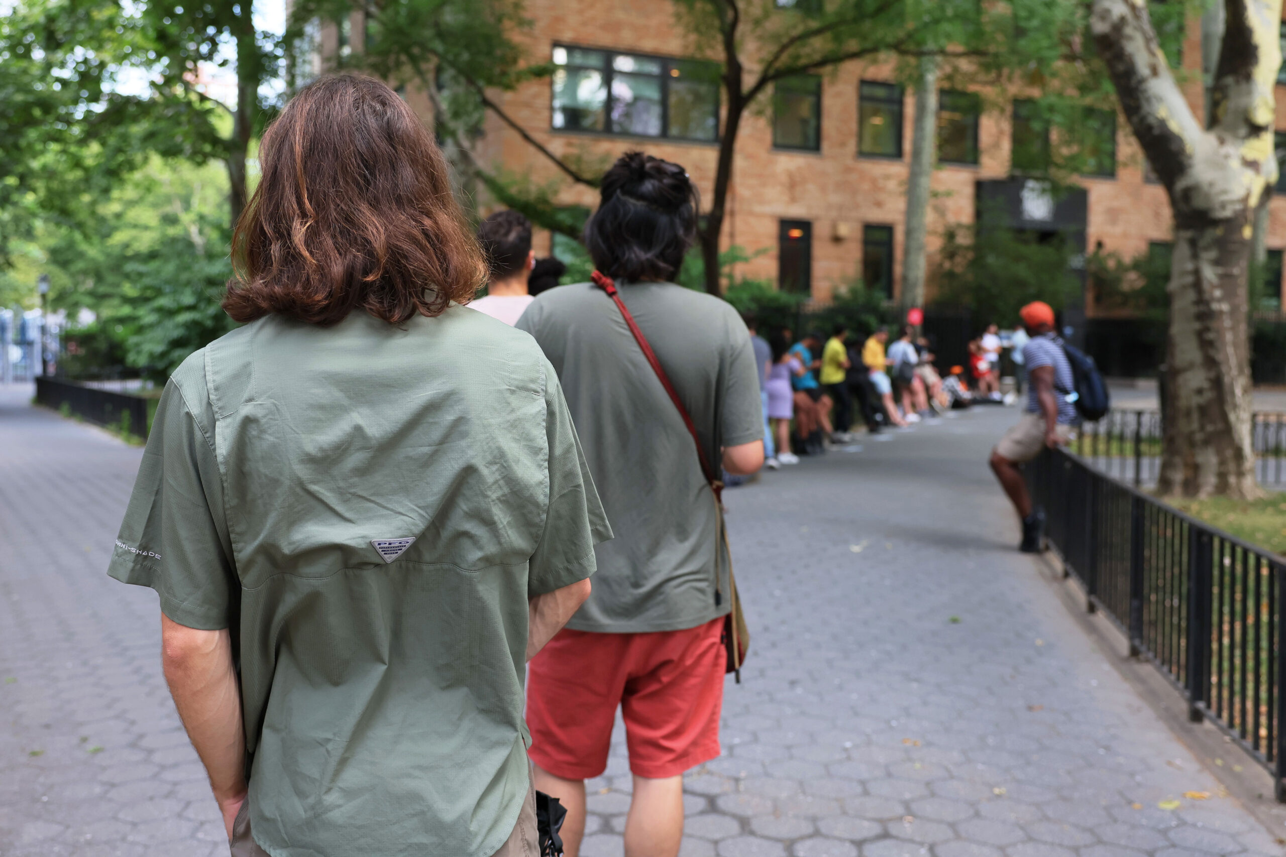 A long line of people facing away from the camera are lined up outside of a building.