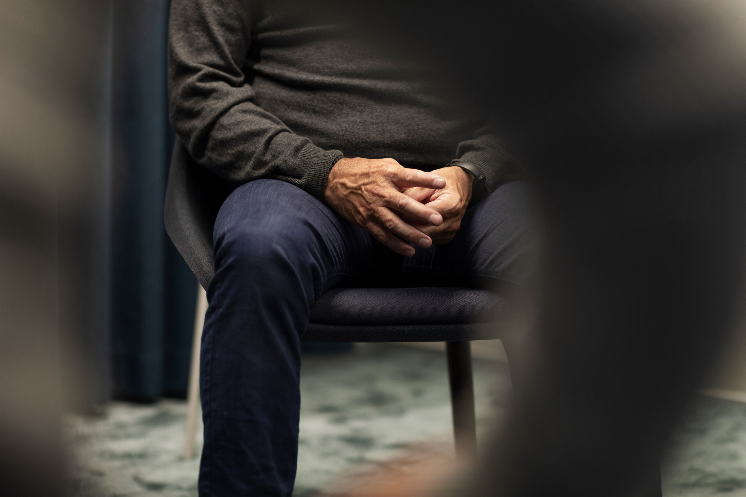 A shows a man's mid-section, sitting in a chair with his hands together.