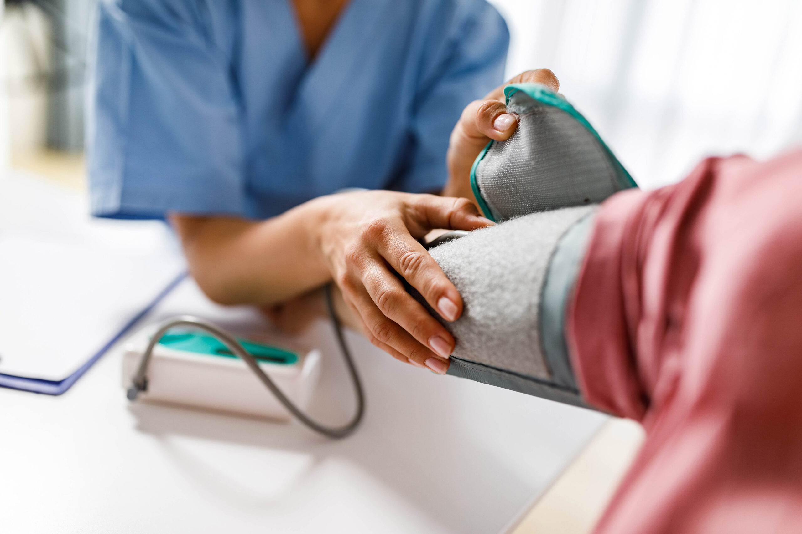 A close up photograph of an unrecognizable female nurse measuring blood pressure of a woman.