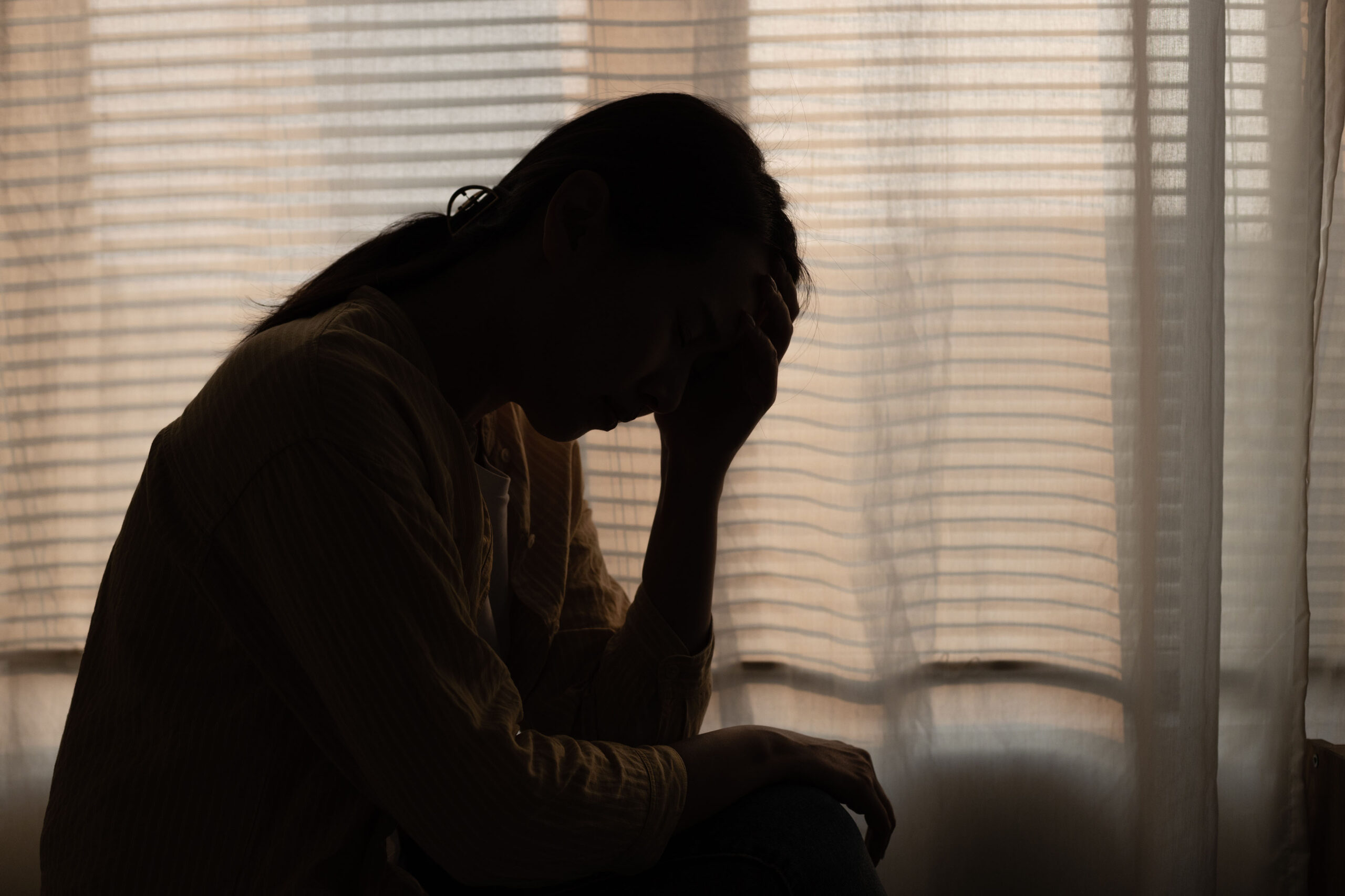 A silhouette of a figure sitting alone in a dark bedroom.